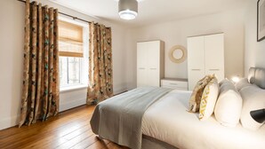 A bedroom with a bed, curtains, a wardrobe, and a bedside table. - Host Stay Wind Rose Cottage (Morpeth)