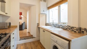 A compact kitchen with a built-in oven, a washing machine, and a sink. - Host Stay Wind Rose Cottage (Morpeth)