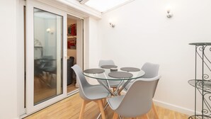 A modern dining area with a glass-top table and grey chairs, a sliding glass door leading to a kitchen, and a small metal side table. - Host Stay Wind Rose Cottage (Morpeth)