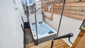 Un jacuzzi en un rincón con terraza de madera y barandillas metálicas.