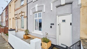 Una hilera de casas escalonadas con puertas delanteras blancas, escalones de madera y pequeños maceteros de madera con plantas.
