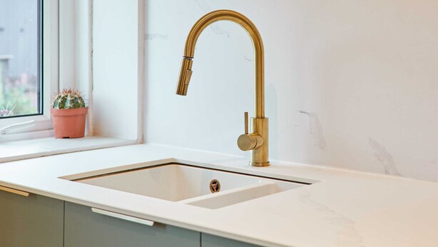 A kitchen with a white countertop, a gold faucet, and a window with a potted plant. - Host Stay Cheviot Street (Wooler)