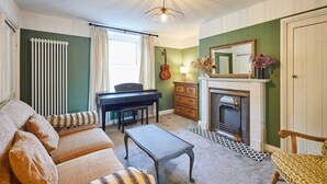 A cozy living room with a piano, sofa, coffee table, and fireplace. - Host Stay Cheviot Street (Wooler)