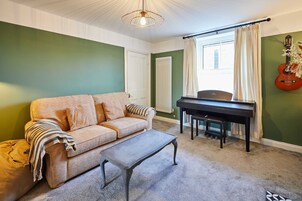 Una sala de estar con un sofá color crema, una mesa de centro, un piano y una guitarra colgada en la pared.