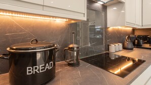 A modern kitchen with a large black slow cooker labeled "BREAD," a coffee maker, and a sleek induction cooktop. - Host Stay High Gables (Northampton)