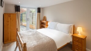 A bedroom with a bed, wooden wardrobe, bedside table, and a view through a glass door to an outdoor area. - Host Stay High Gables (Northampton)