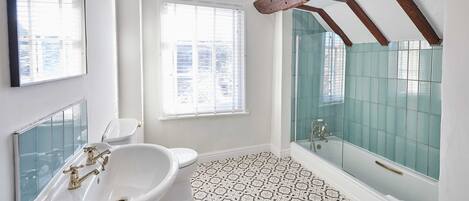 Une salle de bain avec un lavabo, des toilettes et une baignoire, le tout agrémenté d’une paroi de douche en verre.