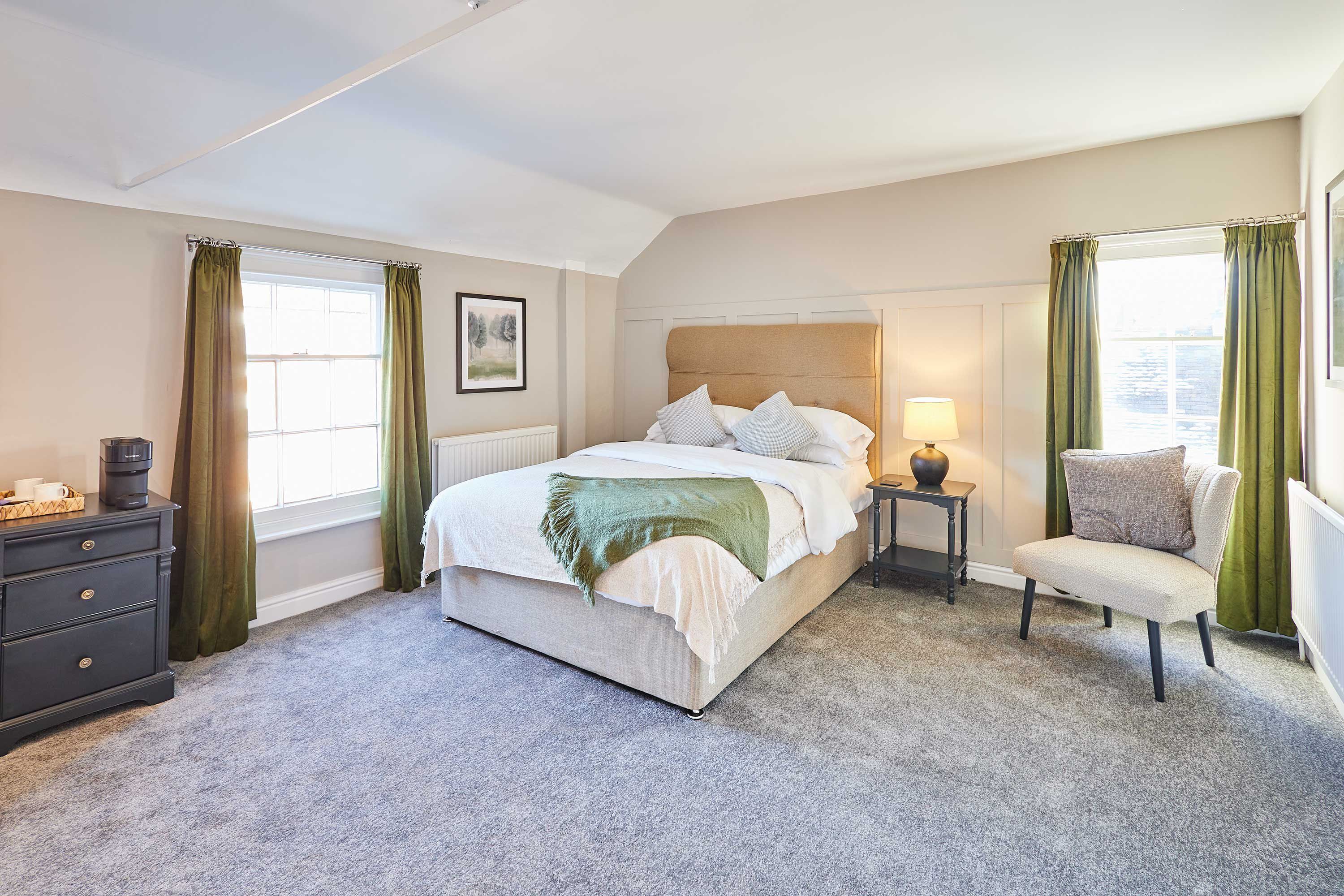 Une chambre à coucher comprenant un lit, une chaise, une table de chevet, une commode et une fenêtre avec des rideaux.