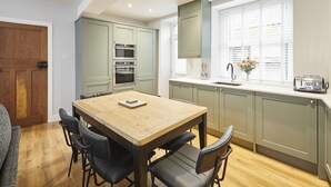 Eine moderne Küche mit Esstisch und Stühlen aus Holz, eingebauten Geräten und einem Fenster mit Jalousien.