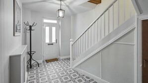 Ein Flur mit gemusterten Bodenfliesen, einem Kleiderständer, einer Tür und einer Treppe mit weißen Geländern.