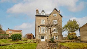 Ein großes, zweistöckiges Steinhaus mit einem markanten Eingang und einer kleinen Veranda.