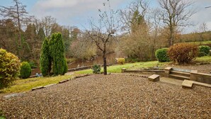 Ein Garten mit Kiesweg, einem kleinen Teich und verschiedenen Bäumen und Sträuchern.