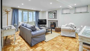 Ein Wohnzimmer mit einer Couch, einem Couchtisch, einem Fernseher, einem Kamin und einem Esstisch.