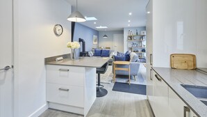 A modern kitchen with a central island, a dining area with a sofa and table, and a living room with a sofa and a coffee table. - Host Stay Harrow Bothy (Berwick-upon-Tweed)