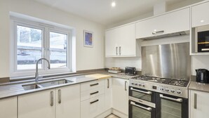 A modern kitchen with a stainless steel stove, oven, and sink. There is a window providing natural light and a view of the outside. - Host Stay Harrow Bothy (Berwick-upon-Tweed)