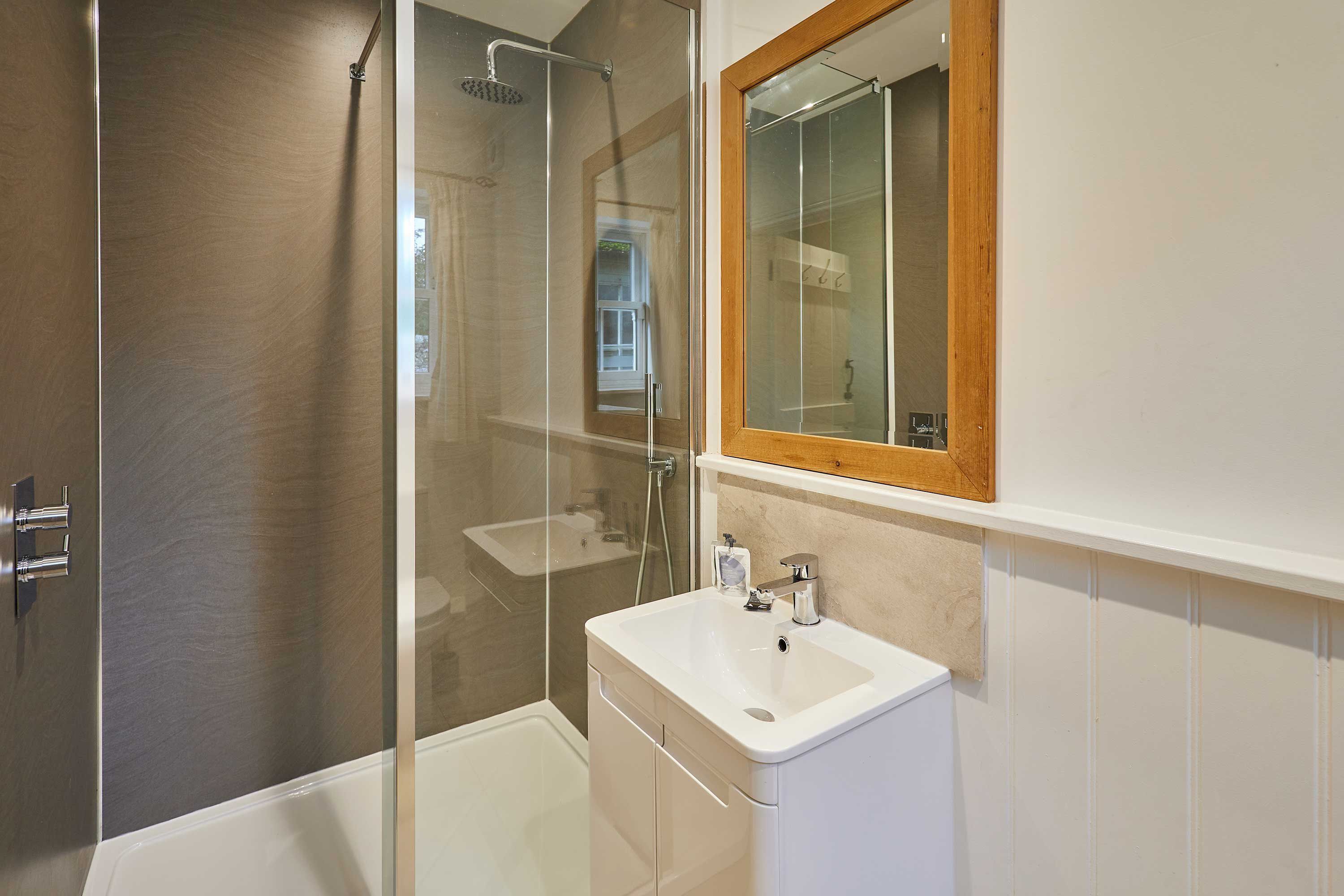 A modern bathroom with a glass-enclosed shower, a white sink, and a wooden-framed mirror.