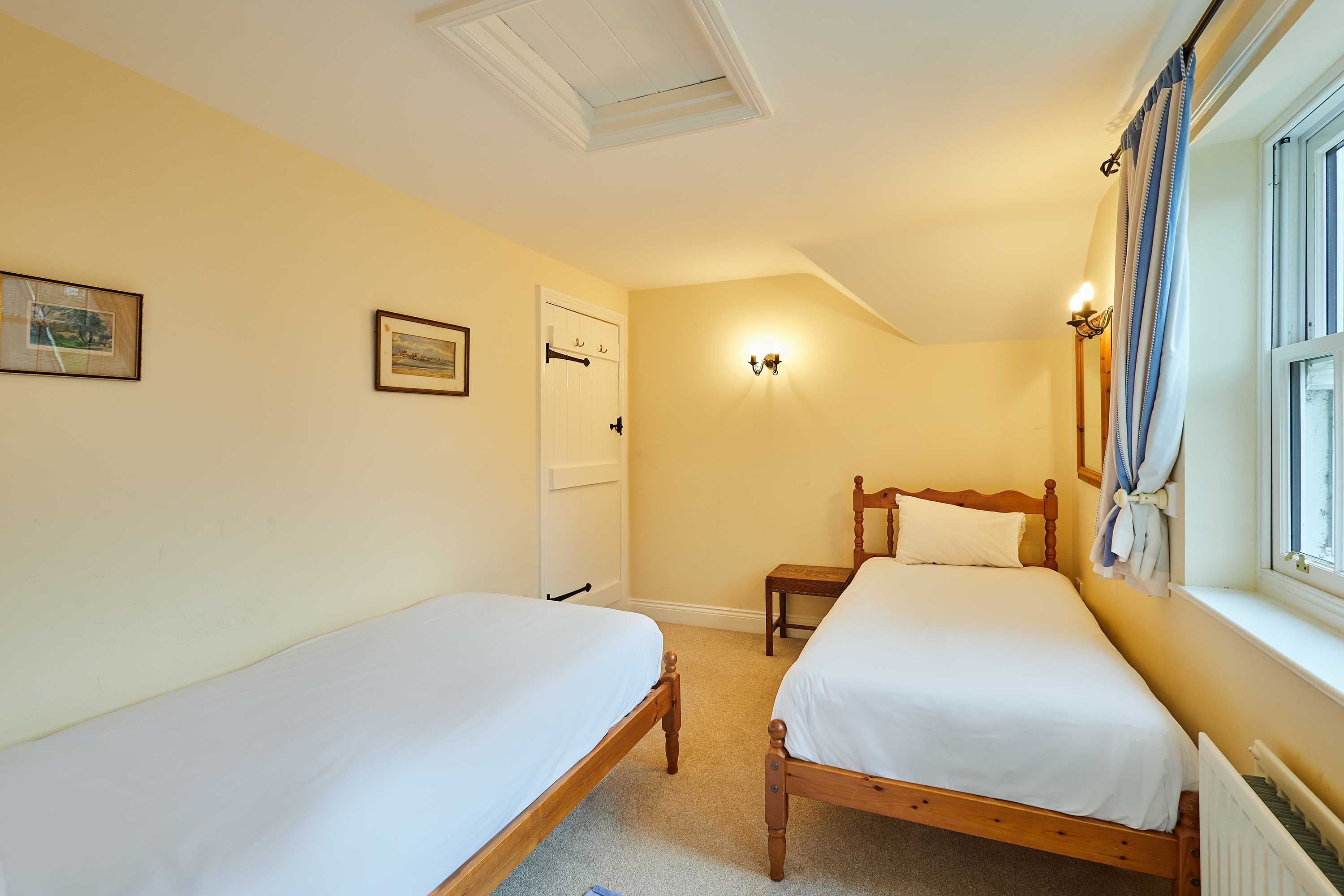 Una camera da letto con due letti in legno, una porta bianca, un comodino e una lampada a parete.