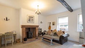 A cozy living room with a fireplace, a sofa, a wooden table, and a bookshelf. - Host Stay Spittal Farm (Wigton)