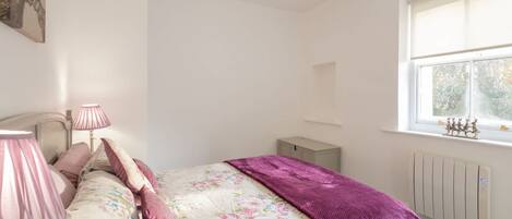 Een slaapkamer met een bed, twee bedlampen, een raam en een radiator.