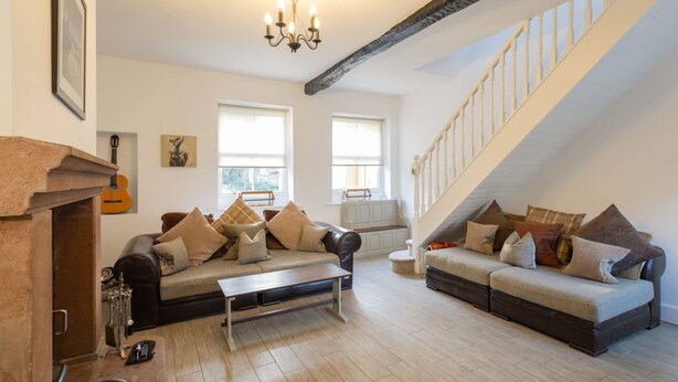 A spacious living room with two sofas, a coffee table, and a fireplace. There is a staircase leading to an upper level. - Host Stay Spittal Farm (Wigton)