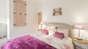 A bedroom with a bed, two bedside tables, a window with wooden shutters, a wall-mounted artwork, and a pink lamp. - Host Stay Spittal Farm (Wigton)