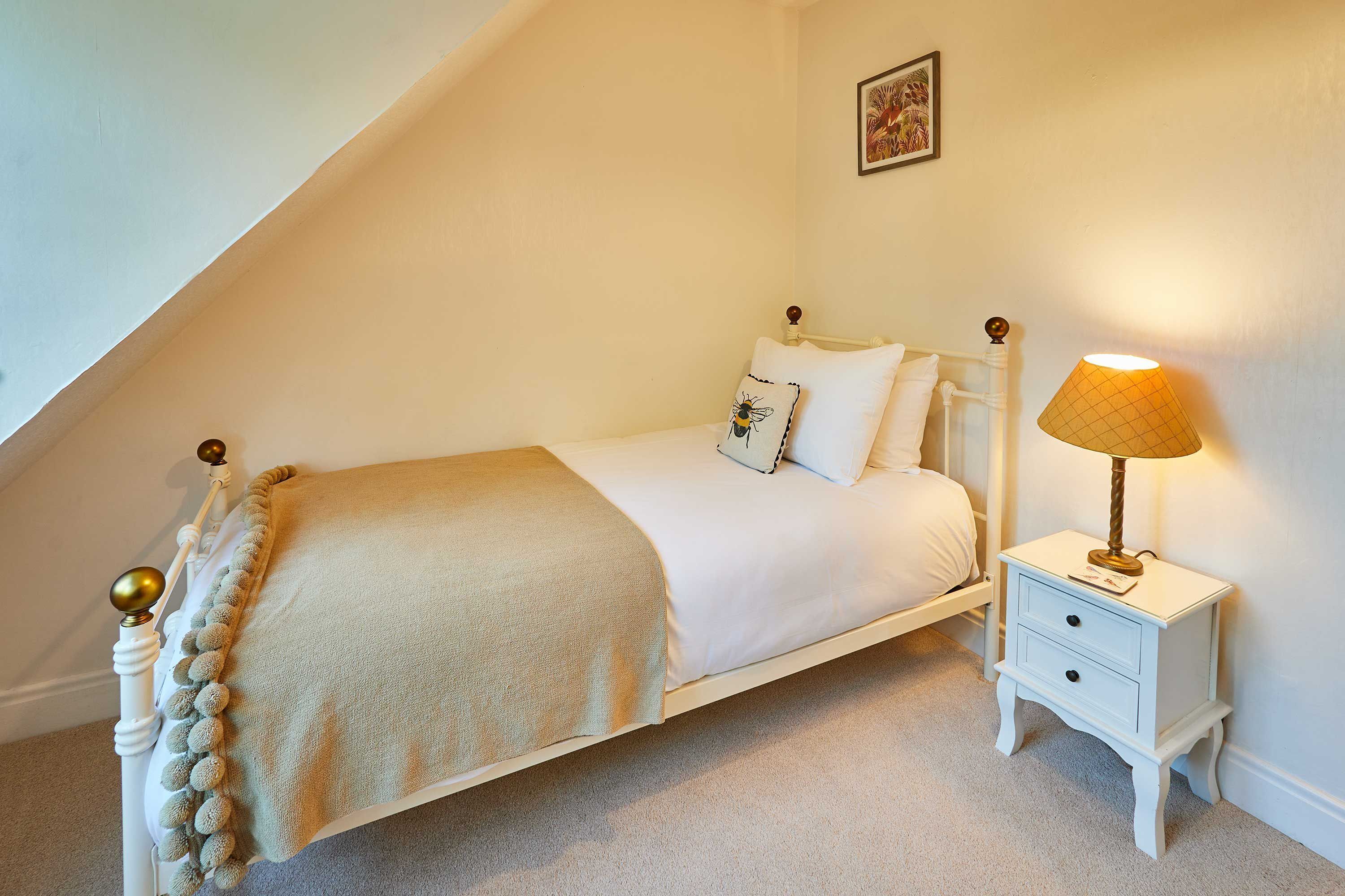 A neatly made bed with a white and beige bedspread, a decorative pillow, and a bedside lamp.
