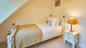 A neatly made bed with a white and beige bedspread, a decorative pillow, and a bedside lamp.