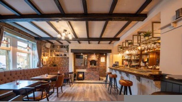 En hyggelig restaurant med synlige træbjælker, en murstenspejs og et barområde med barstole.