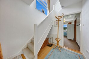 Un escalier avec une rampe en bois, un tapis bleu et une vue sur une cuisine et un espace extérieur.