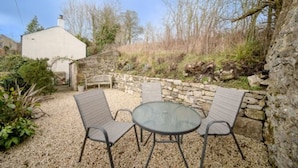 A patio with two metal chairs and a glass table, surrounded by a stone wall and a garden. - Host Stay White House (Matlock)