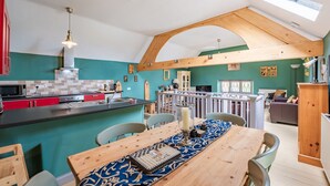 A modern kitchen with red cabinets, a black countertop, and a wooden dining table with a blue table runner. - Host Stay Nine Ladies (Matlock)