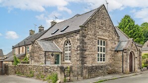 A stone building with a pitched roof, a visible chimney, and a small arched entrance. - Host Stay Nine Ladies (Matlock)