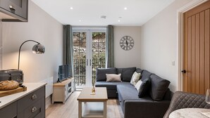 Ein modernes Wohnzimmer mit einem grauen Sofa, einem Holztisch und einem Fernseher auf einem Schrank.