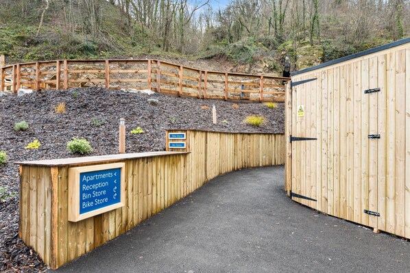 A wooden pathway leading to a building with a sign indicating the locations of apartments, reception, bin store, and bike store. - Host Stay Rock Mill 27 - Chatsworth (Hope Valley)