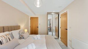 Ein modernes Schlafzimmer mit einem großen Bett, Holztüren und einem durch eine offene Tür einsehbaren Badezimmer.