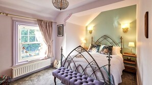Een slaapkamer met een bed, nachtlampjes, een bankje, een raam met gordijnen en een radiator.