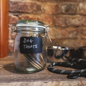 A glass jar labeled "Dog Treats" on a wooden surface with a metal bowl and a leash in the background. - Host Stay 44 Wellington Street (Matlock)