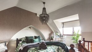 A bedroom with a sloped ceiling, a bed with a leaf-patterned bedspread, a hanging chandelier, and a view of the outside through a window. - Host Stay 44 Wellington Street (Matlock)