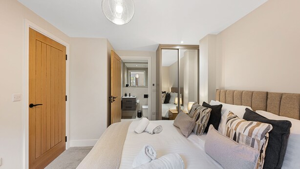 A hotel room with a large bed, a wooden door, a mirror, and a hallway leading to a bathroom. - Host Stay Rock Mill 37 Cavendish (Hope Valley)