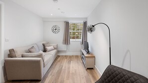 A modern living room with a sofa, TV stand, and a lamp. - Host Stay Rock Mill 37 Cavendish (Hope Valley)
