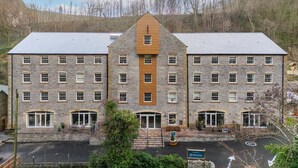 A large stone building with a central wooden section, multiple windows, and a parking area in front. - Host Stay Rock Mill 37 Cavendish (Hope Valley)