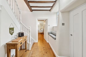 A hallway with a wooden floor, white walls, a bench, a desk with a computer, and a door.