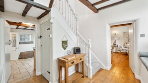 A wooden console table with drawers, a staircase with white balusters, and a herringbone-patterned floor.
