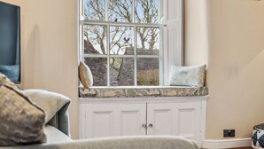 A cozy room with a large window, a built-in bench with cushions, and a television on the left.