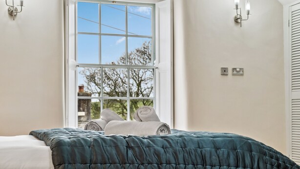 A bedroom with a large window, a bed with a teal duvet, and two wall-mounted light fixtures.