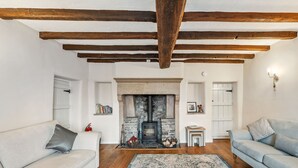 A living room with a fireplace, wooden beams, a sofa, and a rug.