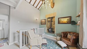 Ein Zimmer mit hoher Decke, einem Chandelier, einem Kamin, einem braunen Ledersofa, einem weißen Sessel und einem gemusterten Teppich.