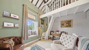Ein gemütliches Wohnzimmer mit hoher Decke, einer Treppe und einem Fenster mit Vorhängen.