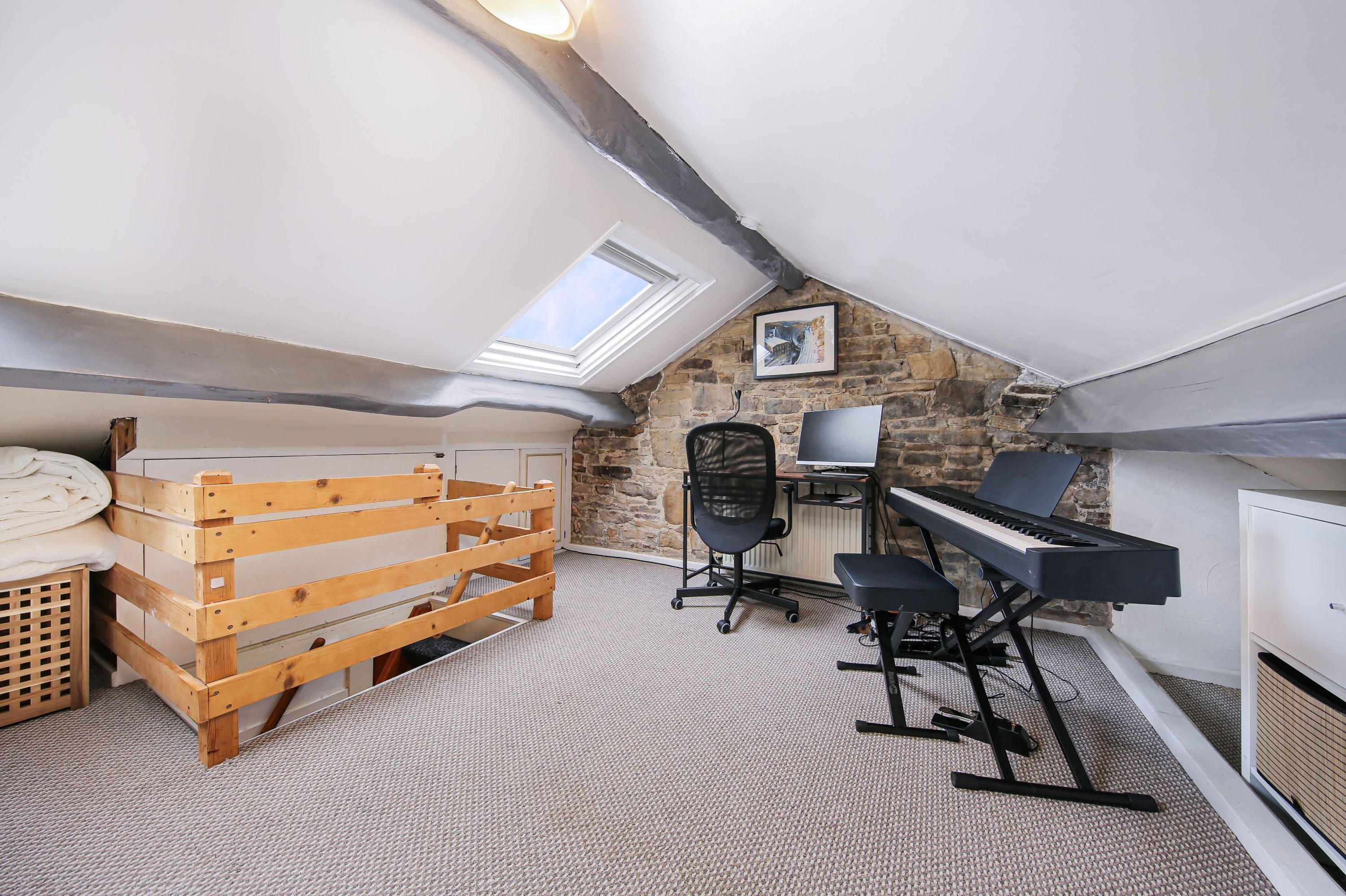 A loft bedroom with a sloped ceiling, a piano, a desk, and a wooden bed frame.
