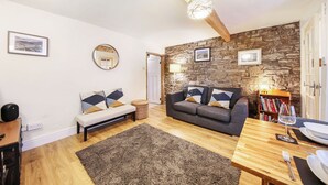 Ein gemütliches Wohnzimmer mit Steinwand, Holzboden und einem grauen Sofa, einem Holztisch und einem Bücherregal.